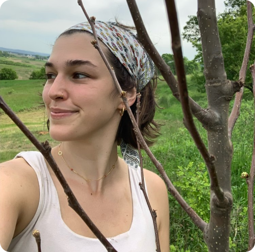 A portrait of Gina, a farm hand at Soil and Soul Farm, standing in a farm field with trees in the background